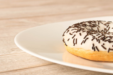 Fresh glazed donut with chocolate sprinkles on a white plate.