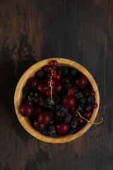 Ripe black and red currants in a wooden bowl on a wooden table. Organic food, harvest season. Top view.