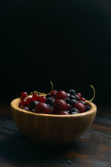 Ripe black and red currants in a wooden bowl on a wooden table. Organic food, harvest season.