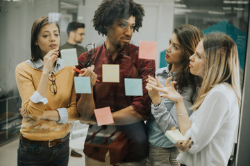 Young business people discussing in front of glass wall using post it notes and stickers