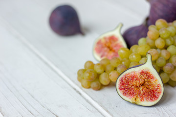 Fresh fruits - figs and grapes over white wooden background.