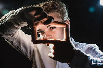 Expressive teenager in a white shirt in bright light, emotional young man with strong hands and beautiful eyes