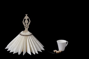 Beautiful white porcelain coffee cup with cane sugar on black saucer and stylized wooden napkin stand on black background. Minimal style. Concept - serving, restaurant, cafe, coffee, decor.