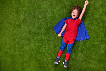 Happy little superhero lying on grass