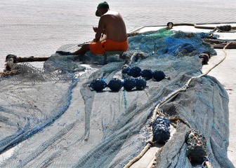 A fisherman sitting in the harbor repairs fishing nets. Traditional fishing concept