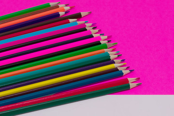 Many colored pencils lie on a white-pink background. Copy spase. The concept of back to school, the educational process, study at school, drawing