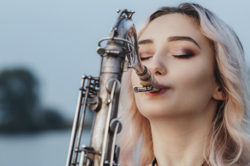Fototapeta na wymiar Portrait of young musician on nature background, woman face playing saxophone and blowing into the trumpet, concept music and relax