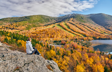 Woman hiking at Artist's Bluff in autumn. View of Echo Lake. Fall colours in Franconia Notch State...