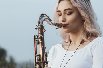 Portrait of young musician on nature background, woman face playing saxophone and blowing into the...