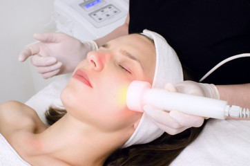 Obraz na płótnie Canvas beautician doing red led light therapy to female customer in beauty salon, facial photo therapy for skin pore cleansing. Anti-aging treatments and photo rejuvenation procedure