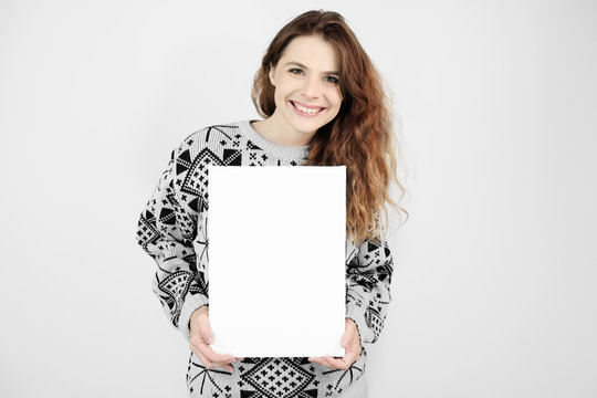 Attractive happy young woman wearing Christmas sweater holding a blank canvas in her hands.