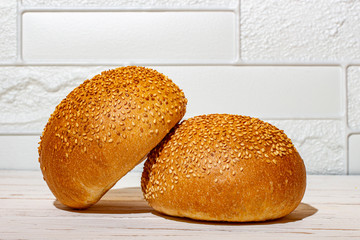 Bun with sesame seeds for a burger on a white wooden background.