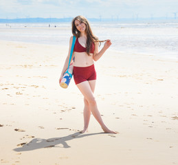 beautiful young woman in a bikini on the beach with a yoga mat
