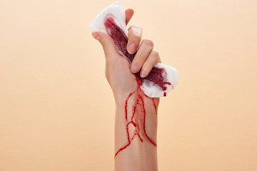 partial view of woman squeezing sanitary towel with blood isolated on beige