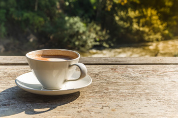 A cup of coffee  on brown desk wood and blur stream view background.
