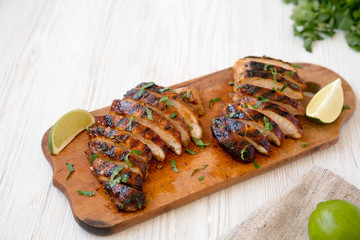 Grilled chipotle chicken breast on a rustic wooden board on a white wooden background, side view. Copy space.
