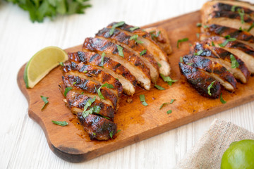 Grilled chipotle chicken breast on a rustic wooden board on a white wooden surface, side view....