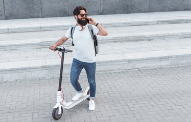 Hipster on electric scooter speaking on smartphone