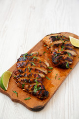 Grilled chipotle chicken breast on a rustic wooden board on a white wooden background, side view. Copy space.