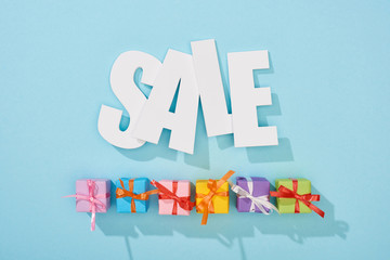 top view of white sale word above festive wrapped presents on blue background