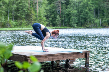 Yogi girl practicing yoga, doing Bakasana exercise, Crane pose,  on the lake.   Concept of healthy life and natural balance
