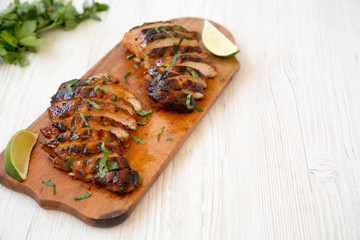 Grilled chipotle chicken breast on a rustic wooden board on a white wooden background, low angle view. Copy space.