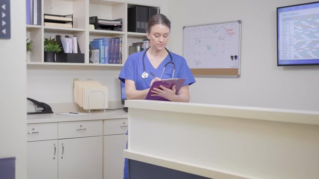 Nurse writing on clipboard as second nurse enters with tablet, camera move left