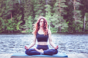 Beautiful girl in a yoga pose on the lake. Lotus position ,  Padmasana. The concept of appeasement,  healthy lifestyle.