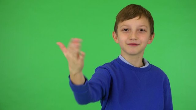 A young cute boy motions to the camera in a gesture of invitation with a smile - green screen studio