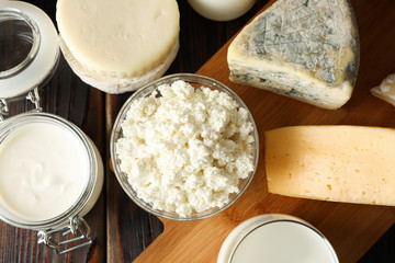 Fresh dairy products and cutting board on wooden background, top view