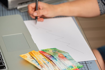 Junge Frau zeichnet eine Gewinnmarge auf einem Blatt Papier. Das Geld liegt daneben.