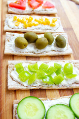 Homemade Crispbread toast with Cottage Cheese and green olives,slices of cabbage,tomatoes,corn,green pepper on cutting board on white concrete background.Healthy food concept,Top view.Flat Lay