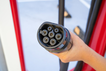  Woman hand holding plug in connector for Charging electric car. Charging an electric car with the...