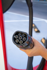 Woman hand holding plug in connector for Charging electric car. Charging an electric car with the...