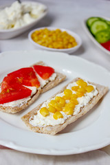 Homemade Crispbread toast with Cottage Cheese and green olives,slices of cabbage,tomatoes,corn,green pepper on cutting board on white concrete background.Healthy food concept,Top view.Flat Lay
