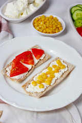 Homemade Crispbread toast with Cottage Cheese and green olives,slices of cabbage,tomatoes,corn,green pepper on cutting board on white concrete background.Healthy food concept,Top view.Flat Lay
