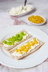 Homemade Crispbread toast with Cottage Cheese and green olives,slices of cabbage,tomatoes,corn,green pepper on cutting board on white concrete background.Healthy food concept,Top view.Flat Lay