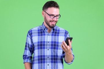 Happy young handsome bearded hipster man using phone