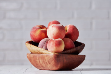 Peaches in wooden bowl with white brick wall background