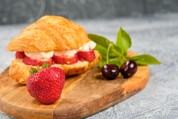 croissant sweet sandwich with cream cheese and strawberries on a wooden board and gray background. Useful breakfast. Proper nutrition. French traditional dishes.