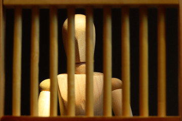 wooden mannequin behind jail bars