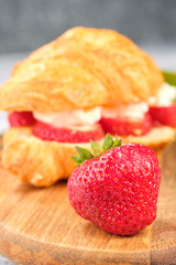 croissant sweet sandwich with cream cheese and strawberries on a wooden board and gray background. Useful breakfast. Proper nutrition. French traditional dishes.
