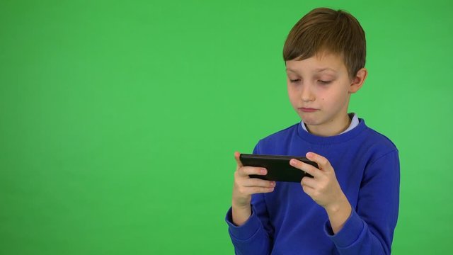 A young cute boy plays a game on a smartphone - green screen studio