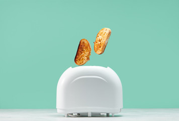 Roasted toast bread popping up of toaster with green wall, front view