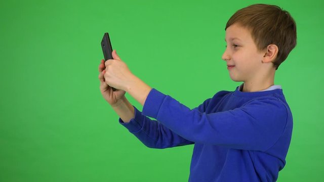 A young cute boy takes selfies with a smartphone - green screen studio