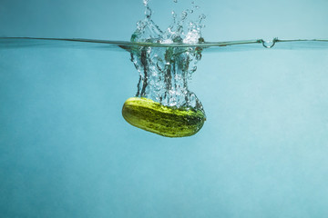 Ripe green cucumber with spray thrown into clear, clear water.