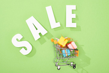 top view of decorative gift boxes in shopping cart near white sale lettering on green background