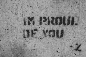 Black-and-white photo of a phrase reading, "I'M PROUD OF YOU" stenciled onto a concrete wall