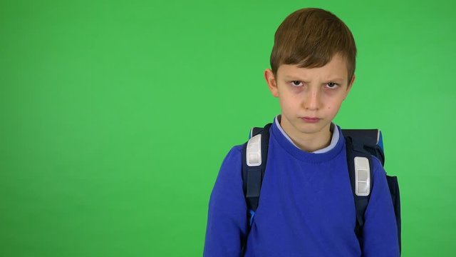 A young cute boy with a schoolbag frowns and shakes his head at the camera - green screen studio