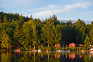 Cabin coastline on Saranac Lake in upstate New York bathed in the morning sunrise. The colored cabins are reflected in the water